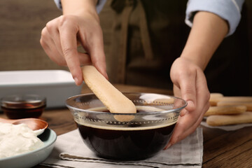 Woman making tiramisu cake at wooden table, closeup