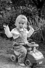 Little girl in denim overalls on driving dad's old car b / w