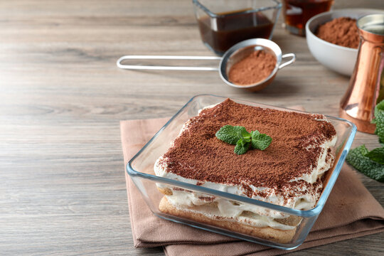 Glass bowl with delicious tiramisu cake on wooden table, space for text