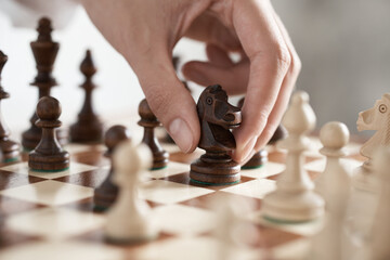 The girl player is holding a horse chess piece in his hand, making a move with a chess piece made of wood. chess game movement of a piece on a chessboard
