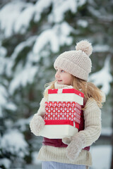Little funny child dressed in Santa Claus red costume bringing presents in winter snowy forest. Christmas Eve 
