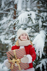 Little funny child dressed in Santa Claus red costume bringing presents in winter snowy forest. Christmas Eve 