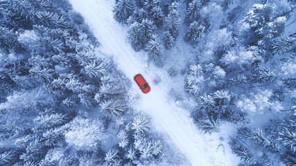 Country road going through the beautiful snow covered forest. Red car driving on winter road. Aerial view. Drone photography.