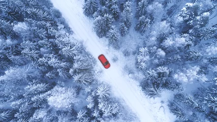 Poster Country road going through the beautiful snow covered forest. Red car driving on winter road. Aerial view. Drone photography. © raland