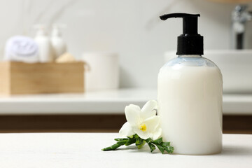Fototapeta na wymiar Dispenser of liquid soap and freesia flower on white table in bathroom, space for text