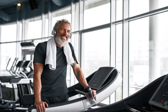 Cheerful grey-haired man with towel around neck, posing in gym
