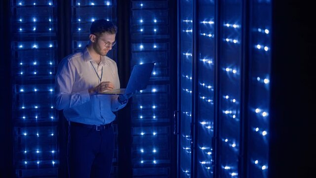 Male Server Engineer in Data Center. IT engineer inspecting a secure server cabinet using modern technology laptop coworking in data center.