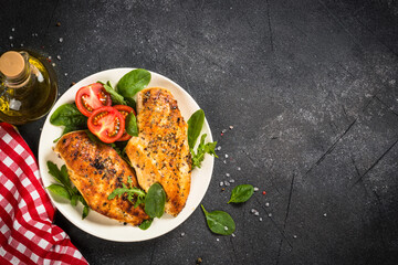 Grilled chicken fillet at with green leaves and vegetables. Top view at black stone table with space for text.