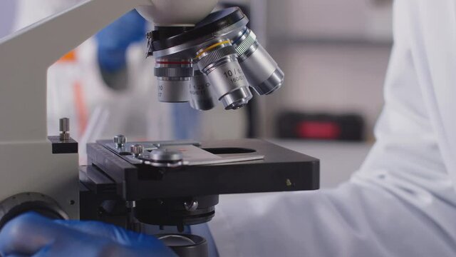 Close Up Of Female Lab Worker Or Phlebotomist Analysing Blood Samples In Laboratory With Microscope
