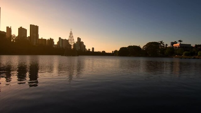 Beautiful lake with few buildings and trees on the background during sunset. Zoom out video. Landscape of Igapo lake at Londrina PR, Brazil.