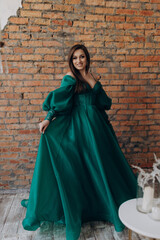 Naklejka premium A beautiful girl in a green dress smile shows a brick wall dress
