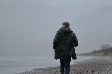 a guy in a black jacket run along the sandy cloudy sea