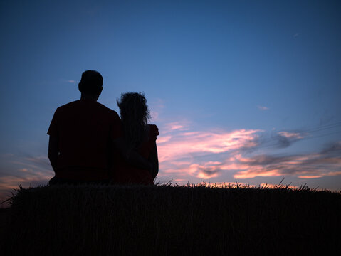 A rear silhouette of a romantic young couple with their dog watching the sunset on the beach
