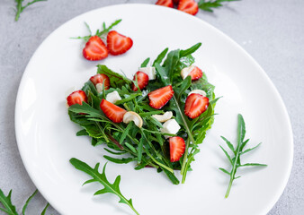 Vegan salad of strawberry with mix of herbs, arugula, spinach leaves, mozarella cheese and cashew nuts in heart shape on white plate. Clean eating, detox and raw food diet.