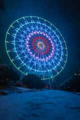 Futuristic amazing neon ferris wheel with bright colored light in a winter park at night with snow....