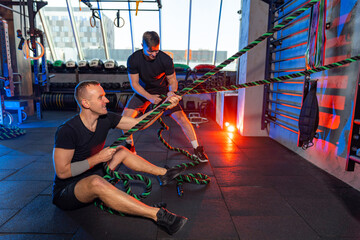 Private instructor helps sporty guy. Young man doing exercises with the help of a TRX suspension strap with a personal trainer in gym