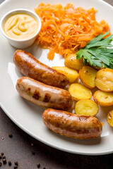 Fried hunter sausage with potatoes, fried cabbage and mustard on white plate on dark brown table macro close up