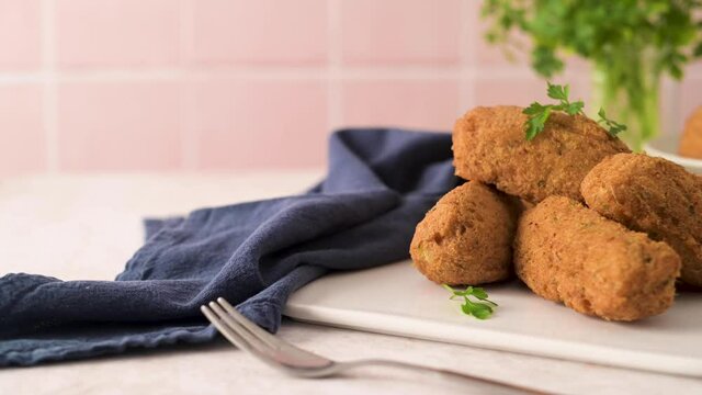 Cod dumplings, or "bolinhos de bacalhau" and parsley leaves on white ceramic dishes in a kitchen counter top.