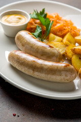bavarian sausages with potatoes and fried cabbage on plate on dark brown concrete table close up