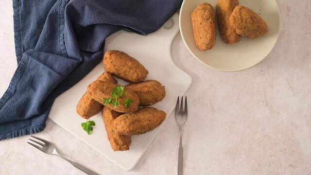 Cod dumplings, or "bolinhos de bacalhau" and parsley leaves on white ceramic dishes in a kitchen counter top.