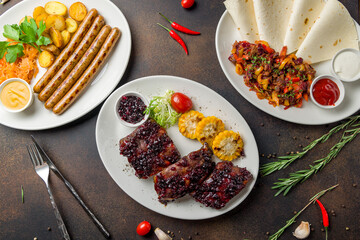 fried pork ribs with lingonberry sauce, fried sausages and fachitos with beef top view on dark brown table