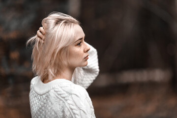 a young blonde in a white sweater straightens her hair with her hand portrait in profile