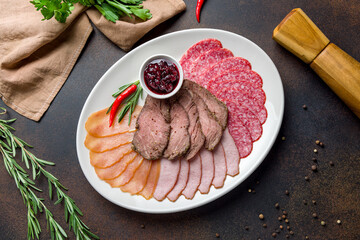 slicing of different meat on plate on dark brown concrete table top view