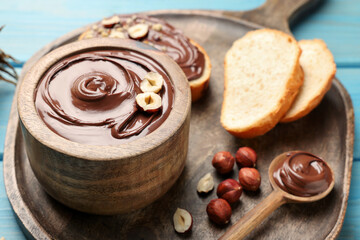 Bowl of tasty chocolate paste with hazelnuts on light blue wooden table, space for text