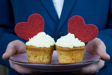 Man in suit holding tasty cupcakes  for Valentine's Day.Male hands holding muffins with red heart as a gift for lover.                   