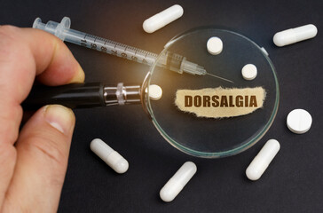 A man looks through a magnifying glass at pills, a syringe and a piece of paper with the inscription - DORSALGIA