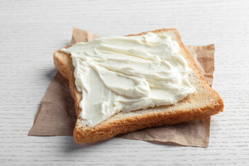Slice of bread with tasty cream cheese on white wooden table, closeup
