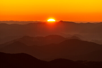 Beautiful sunset above mountains; the forest at orange sunset
