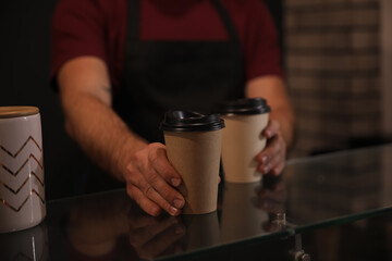Barista putting takeaway coffee cups on glass table indoors, closeup