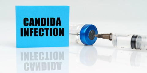 On a white reflective surface are a syringe, an injection and a blue plaque that says - Candida...