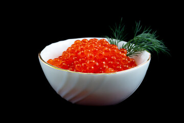 Red salmon caviar with green fennel in a porcelain white bowl isolated on a black background.