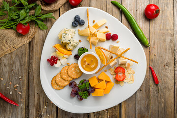 Cheese plate italian food with different cheeses, honey and fruits on white plate on wooden table top view