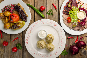 Khinkali with lamb, different sliced meat plate, grilled vegetables on plate top view on wooden table