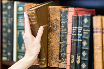 Frau greift altes Buch aus Bücherregal