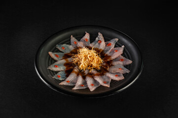 Fish carpaccio in a black plate with sweet potato straws.