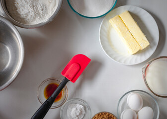 Looking down on ingredients for baking a basic chocolate cake.  Ingredients include flour, sugar, butter, milk, eggs, cocoa, baking powder, and vanilla.  Arranged in swirl pattern.