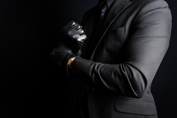 Portrait of Strong Man in Dark Suit Pulling on Black Leather Gloves Menacingly. Concept of Mafia Hitman or Gentleman Assassin. - obrazy, fototapety, plakaty
