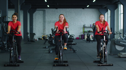 Woman coach engaged spin on stationary bike with group of people in gym. Athletic girls performing...