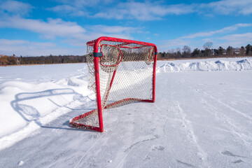 A hockey net Ontario Canada sits on the ice of a pond on a cold blue sky day.