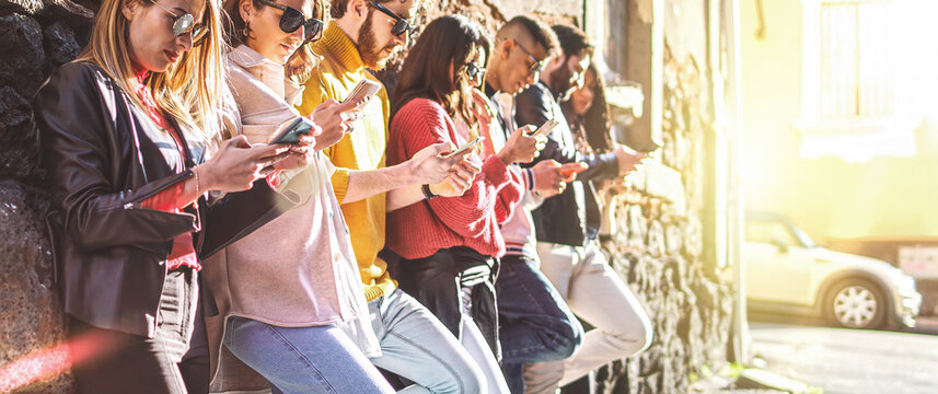 Multicultural group of digital addicted people using smartphone together standing against a wall