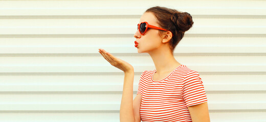 Portrait of stylish young woman blowing her lips sending sweet air kiss with red lipstick wearing a...