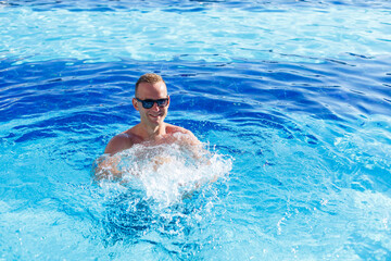 Young attractive man in sunglasses is resting in the pool on summer vacation. The guy in the pool by the hotel