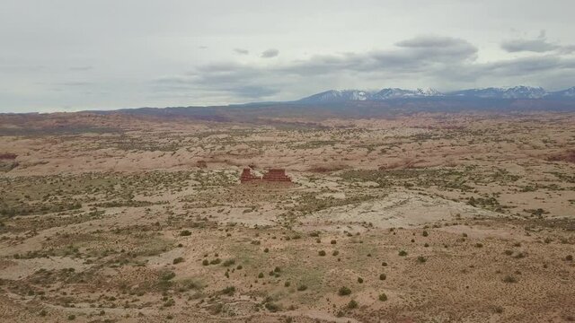 A red rock formation in a desert with snowy mountains behind in Utah