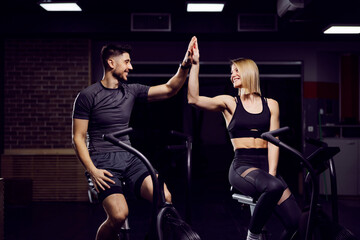 Fototapeta na wymiar Sporty couple on exercise bikes in a gym accomplished a goal. Teamwork concept.