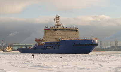 Fototapeta premium A fisherman catches fish on a frozen river and looks at the ships. Winter navigation on the river. Ice fishing.