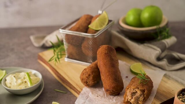 Meat croquets with rosemary leaves and lemons on wooden cutting board in a kitchen counter top.